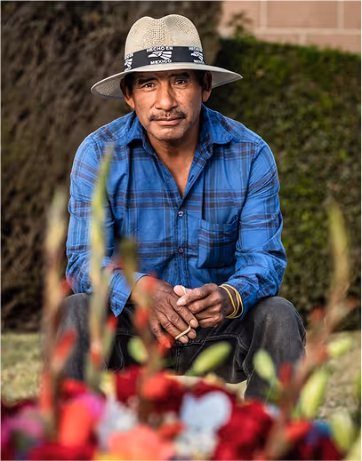 Man wearing a hat seated in a garden with flowers – Throwback Thursday photo.