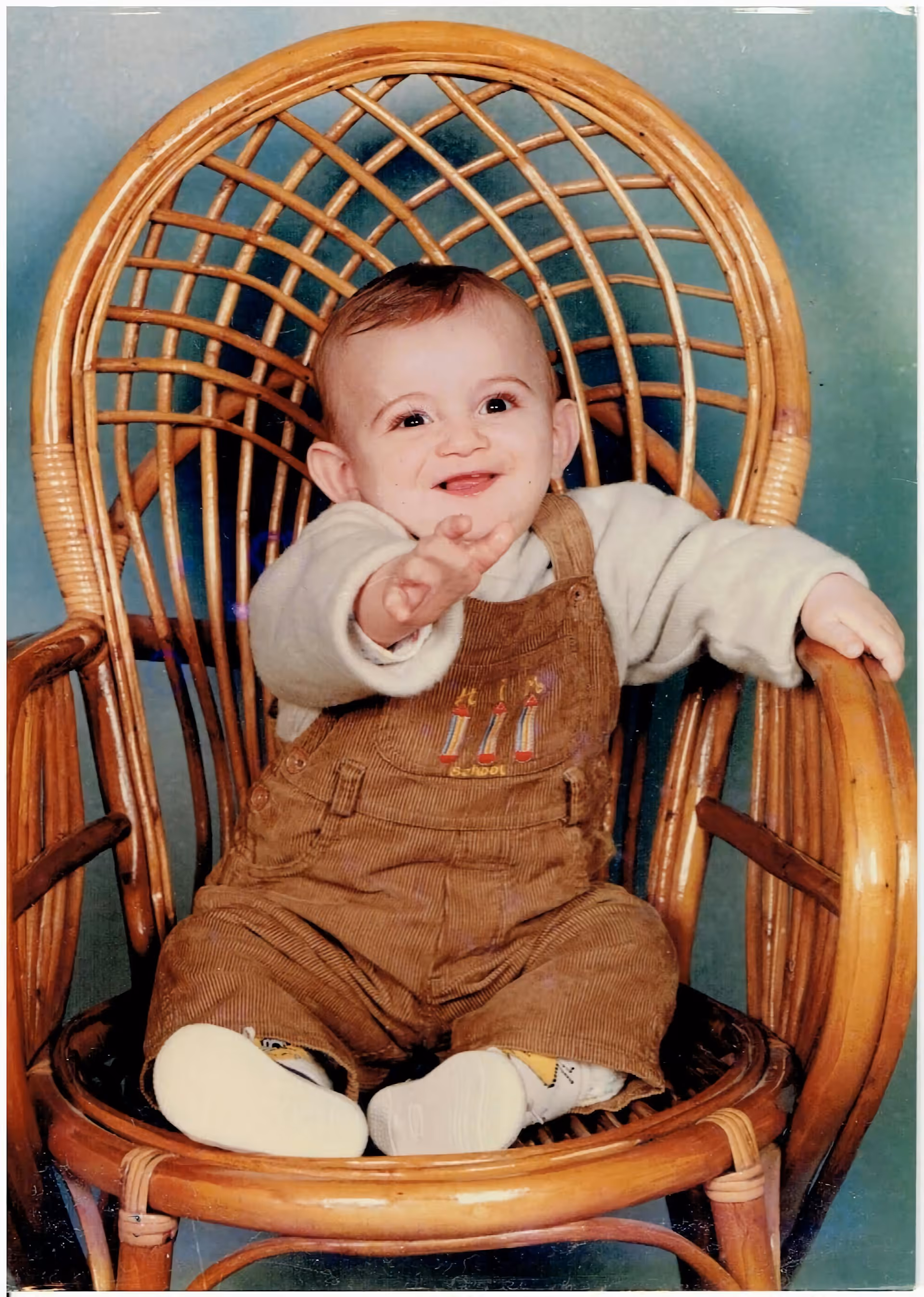 Child sitting in a wicker chair pointing at the camera – Throwback Thursday photo.