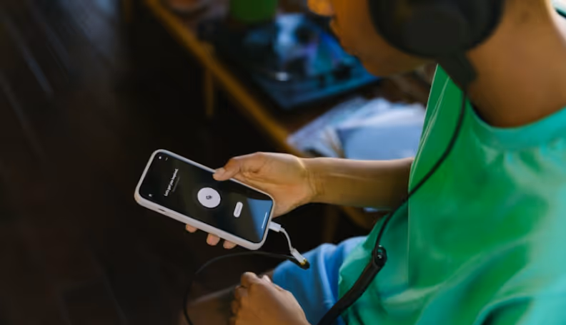 Person wearing headphones holding a smartphone displaying a music playback screen with earbuds connected.