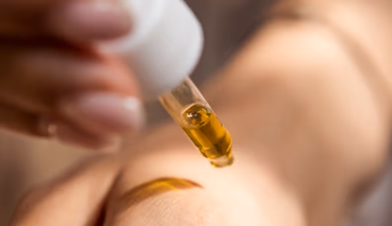 Close-up of a dropper dispensing golden oil onto a person's skin.