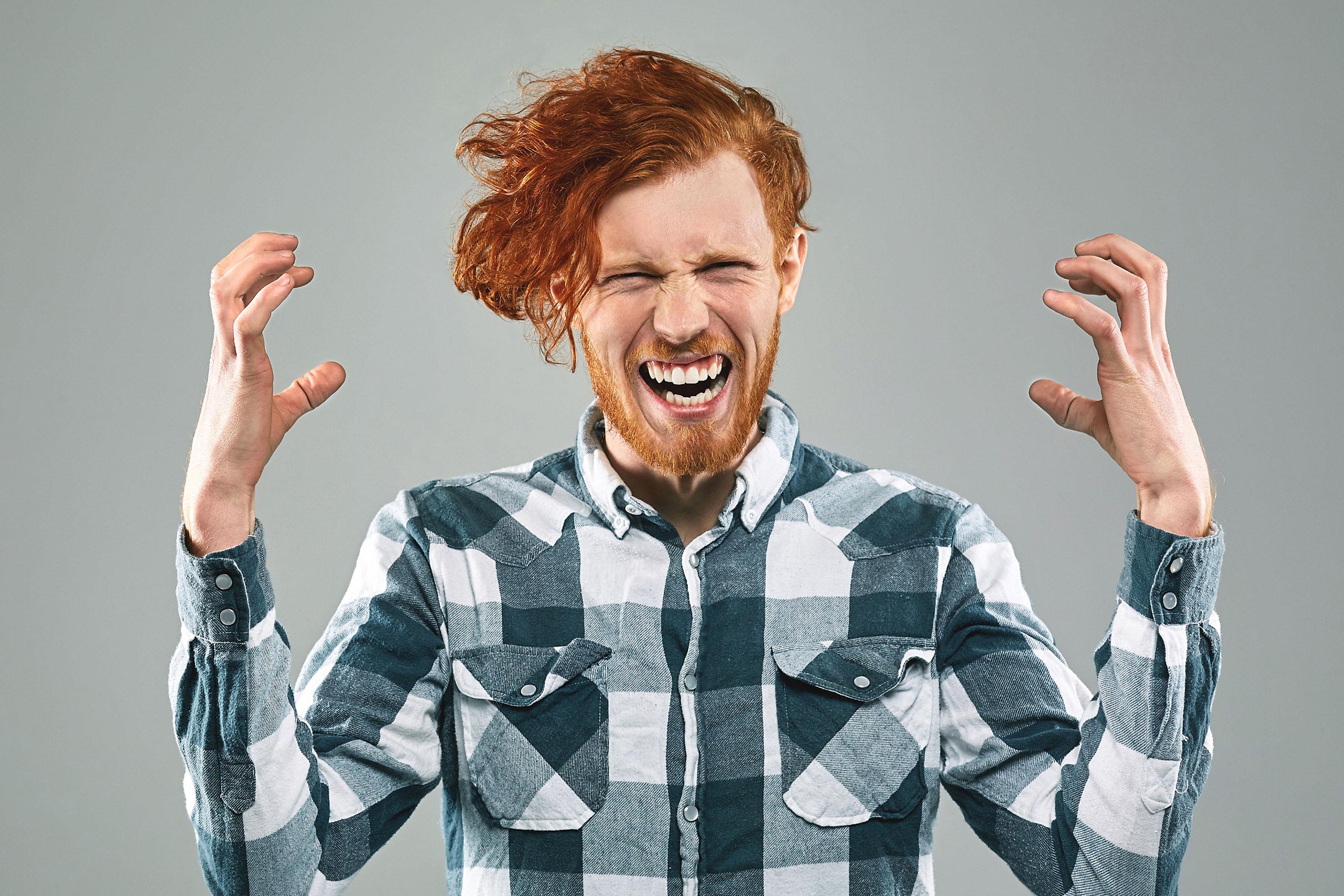 Red-haired man with beard wearing a checkered shirt gestures angrily with clenched hands and eyes closed.