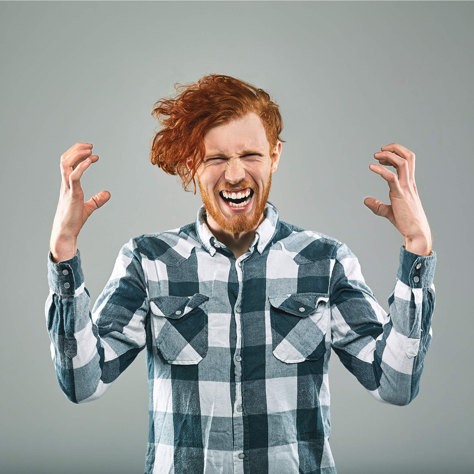 Red-haired man in a checkered shirt with eyes closed and hands raised, expressing frustration or anger.