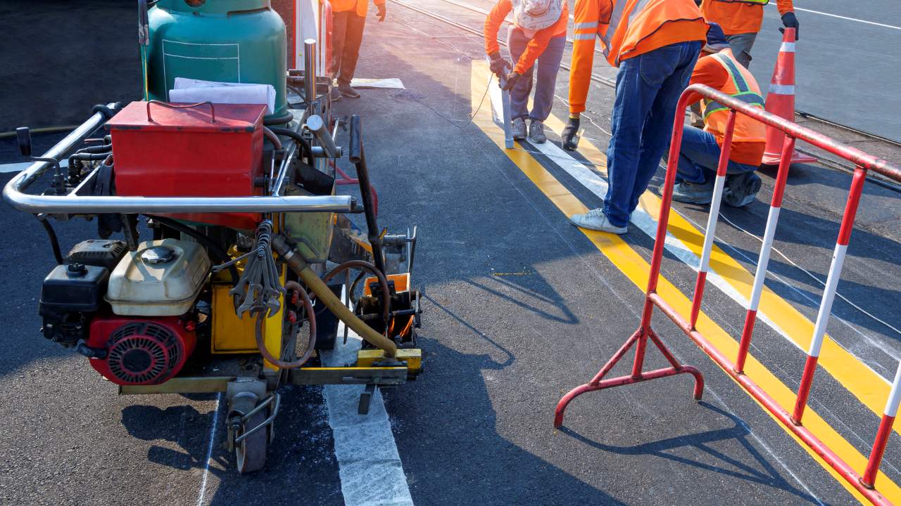  Road workers group with thermoplastic spray road marking machine are working to paint traffic lines on asphalt road