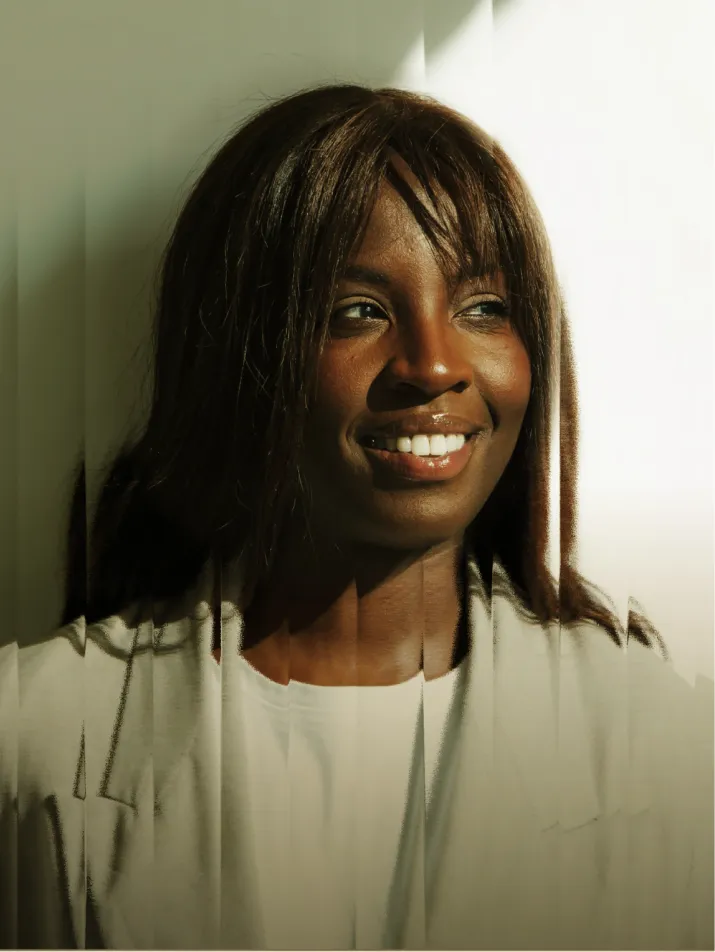 Portrait d'une femme souriante avec des cheveux bruns éclairée par une lumière douce sur fond blanc.