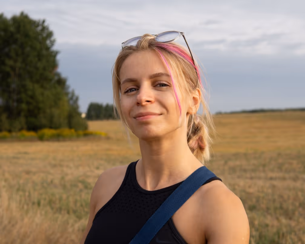 Young woman with blonde hair and pink streaks wearing sunglasses on head in a field.