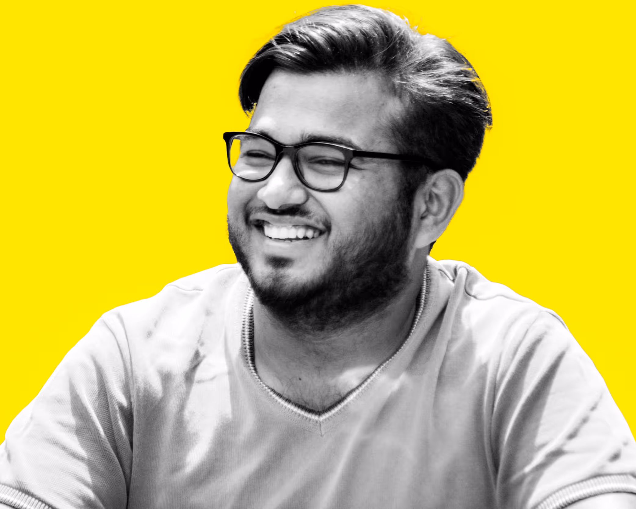 Smiling man with glasses and beard in a grey T-shirt against a bright yellow background.