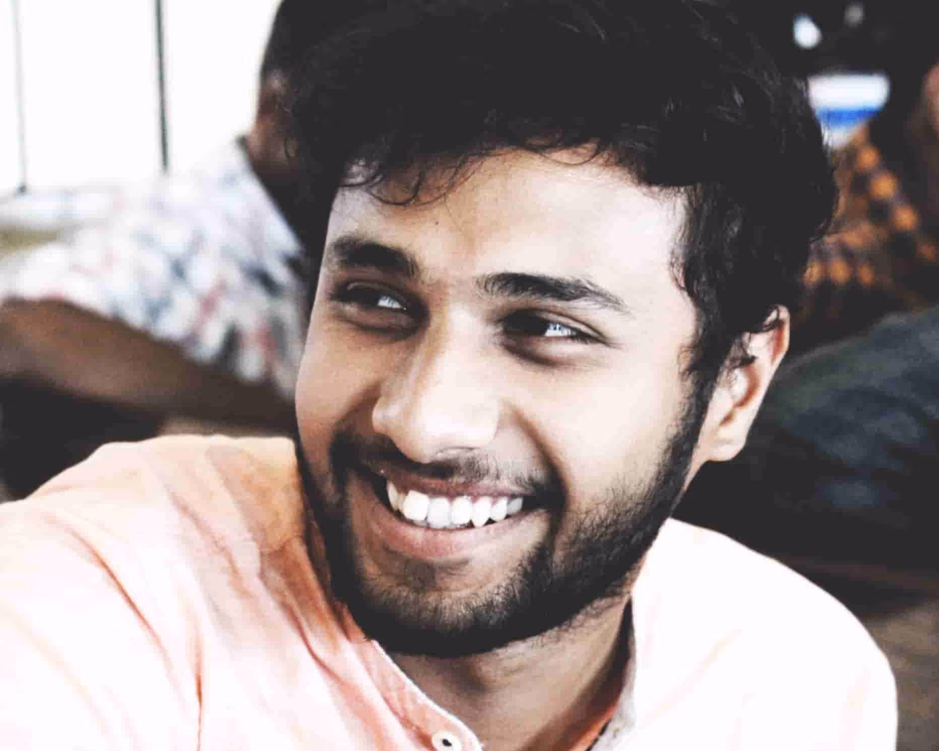 Close-up of a smiling young man with beard and curly hair looking to his left.
