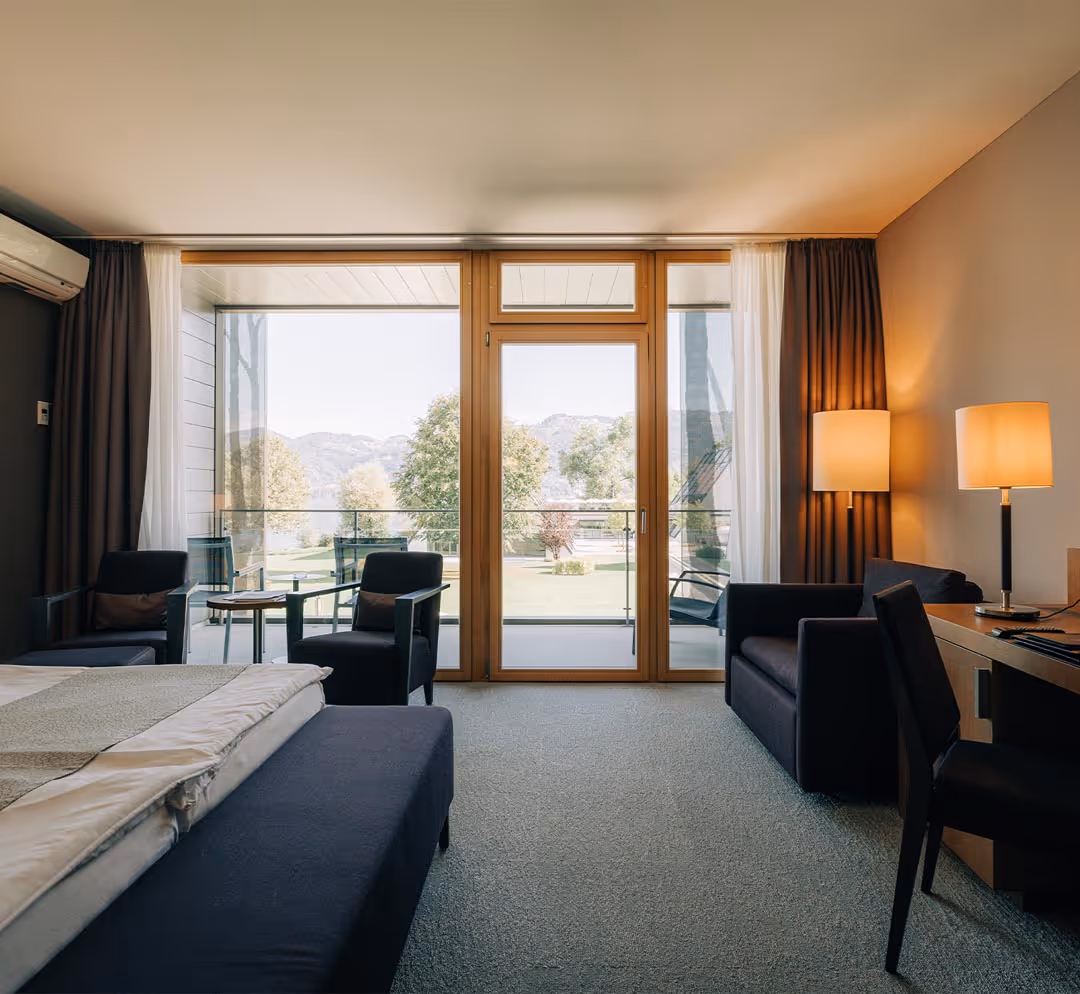 Room with double bed, desk, sitting area, balcony with lake view on Lake Thun