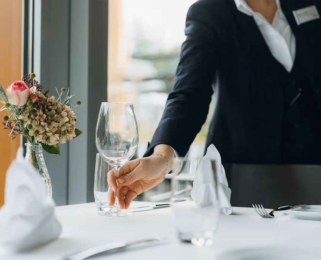 Restaurant specialist sets wine glasses at the table in the Delta restaurant on Lake Thun