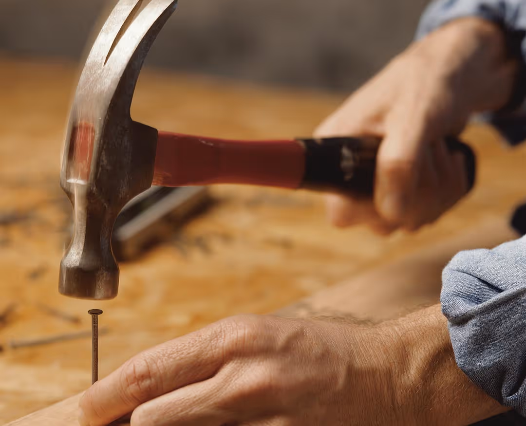 Man drives a nail into wood with a hammer