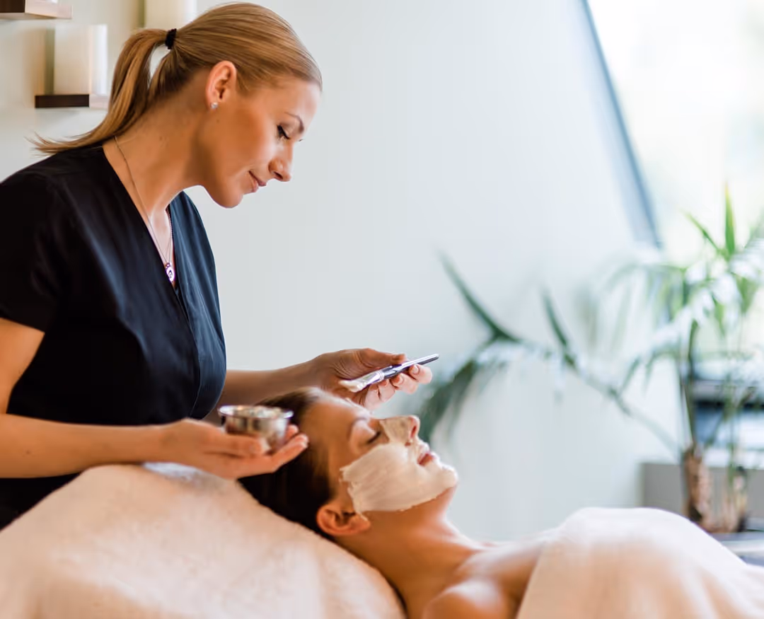 Kosmetikerin des Deltapark Vitalresort trägt eine Gesichtsmaske bei der Kundin auf