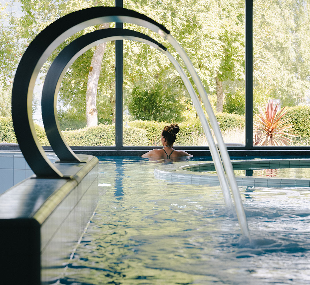 Lady in the indoor saltwater pool with a view of the greenery at the Deltapark Vitalresort