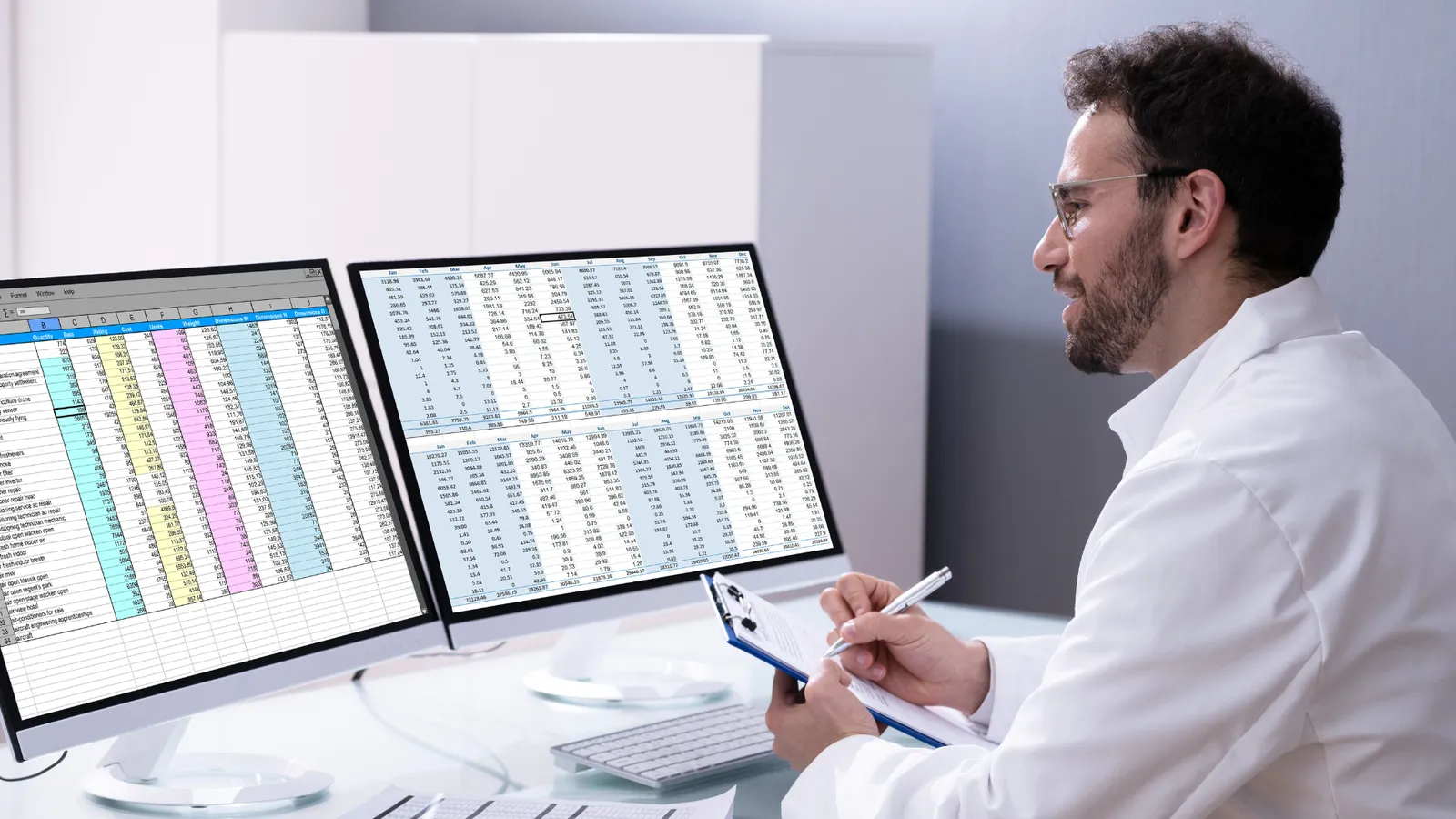 Doctor reviewing billing spreadsheets on two computer monitors