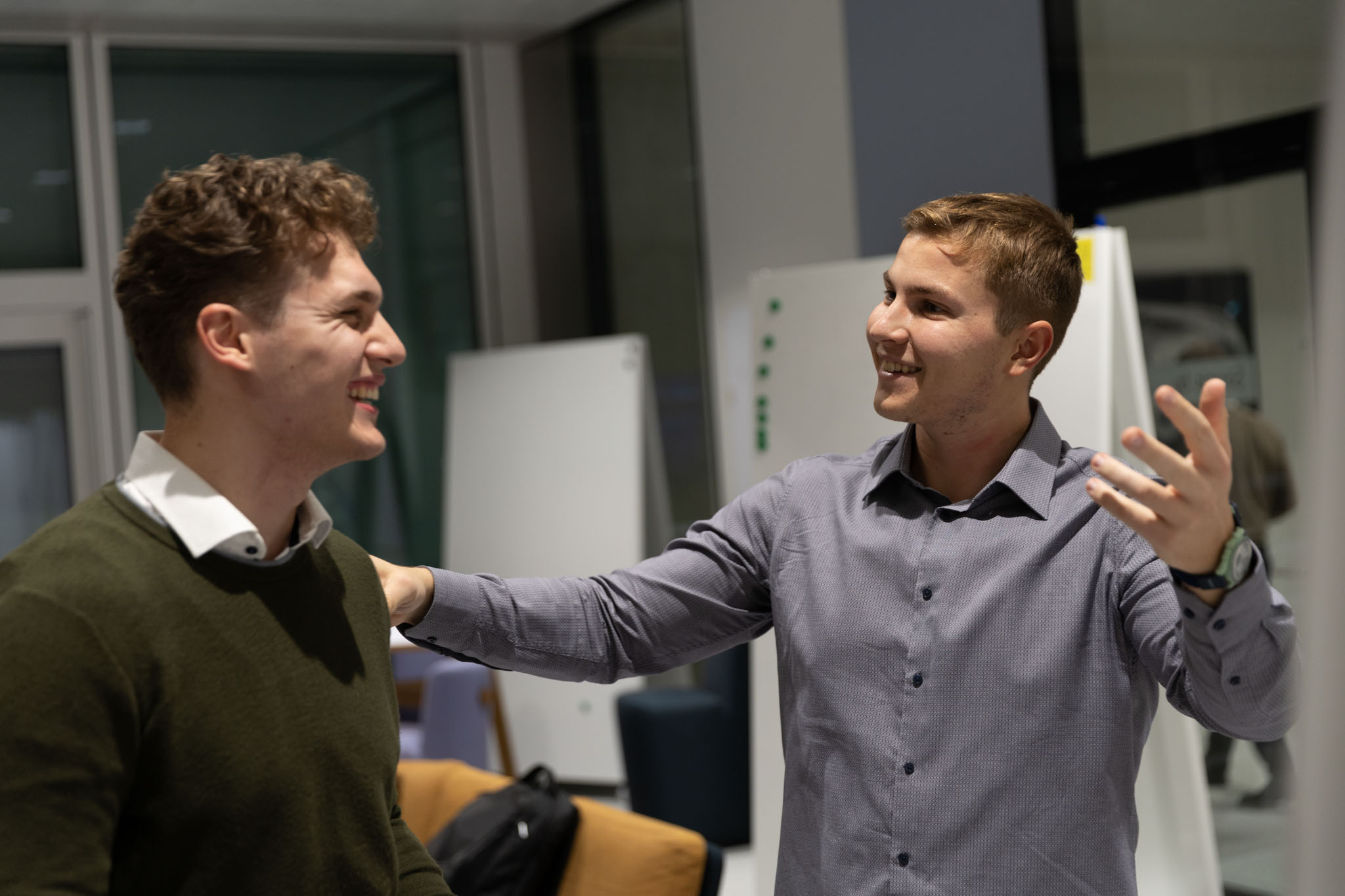 Two people having a professional conversation at a round table in a bright office with plants.