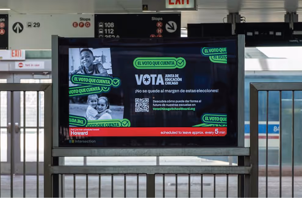 Chicago train station digital sign promoting voting for Chicago Board of Education with images of children and text in Spanish urging participation in elections.