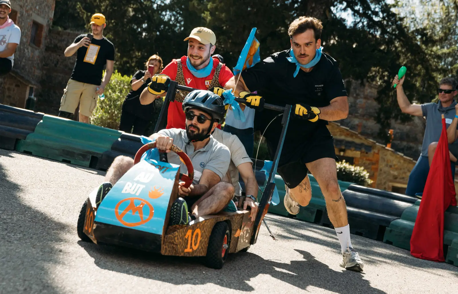 Un homme poussant un kart sans moteur avec deux passagers dans une course de karting amateur en plein air.
