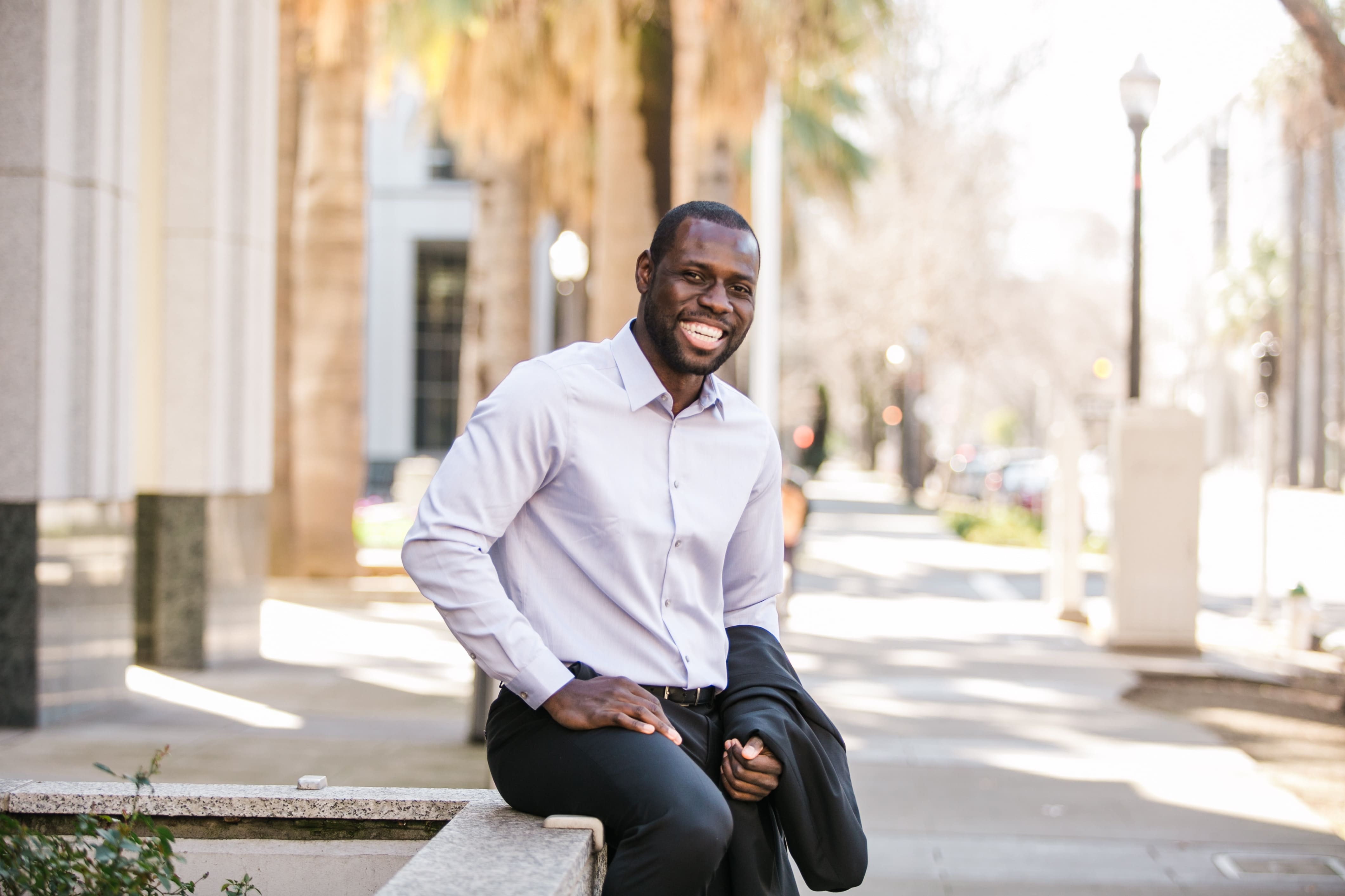 Black man sitting outside on the bench in the sity smilling to a camera objective