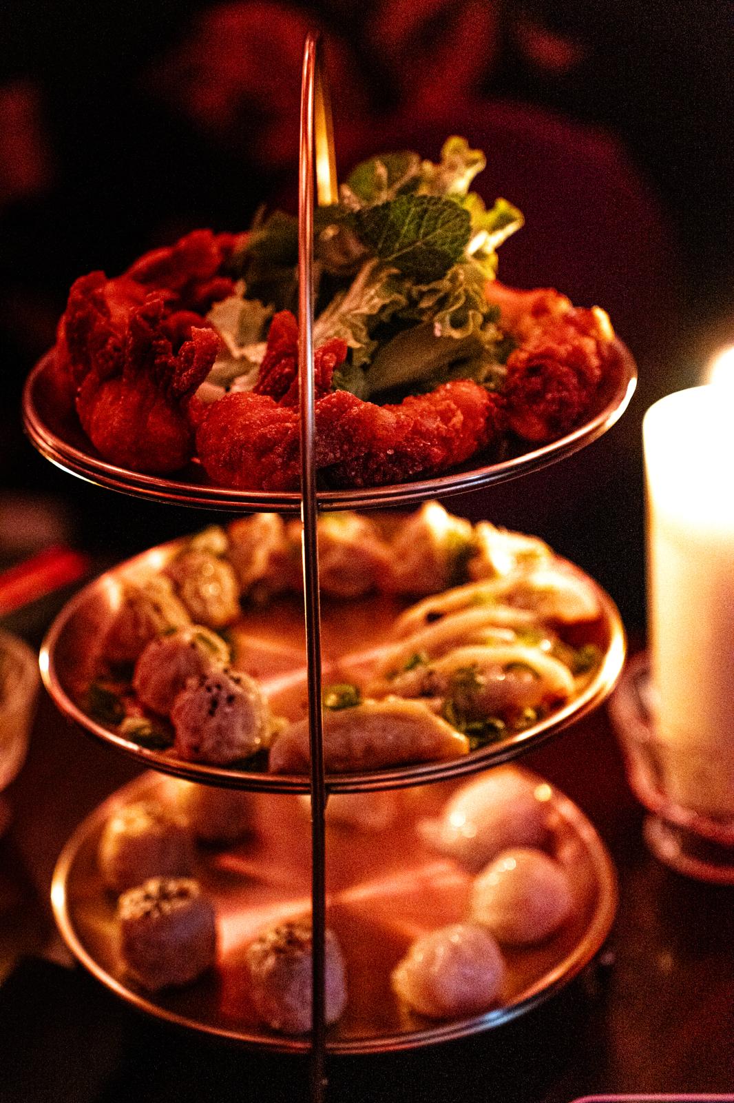 Three-tiered serving tray with fried shrimp, dumplings, and round dim sum under warm candlelight.