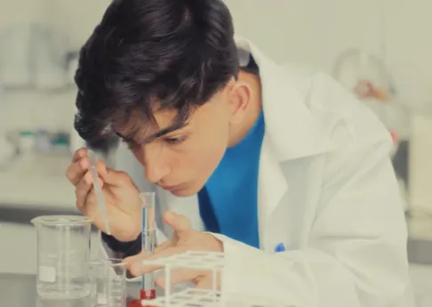 Young scientist wearing white lab coat carefully using a pipette with test tubes in a laboratory.