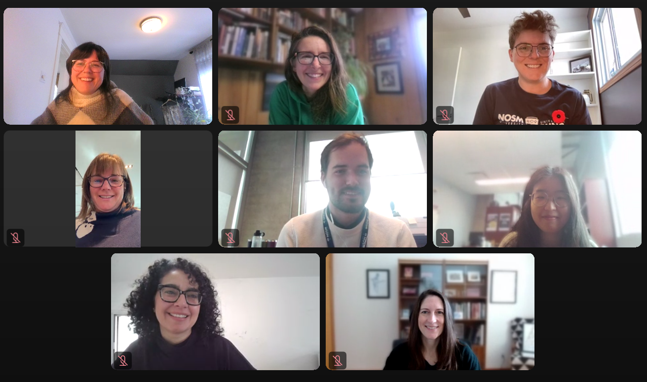 A team photo; 12 team members sitting and standing in front of a wooden wall.