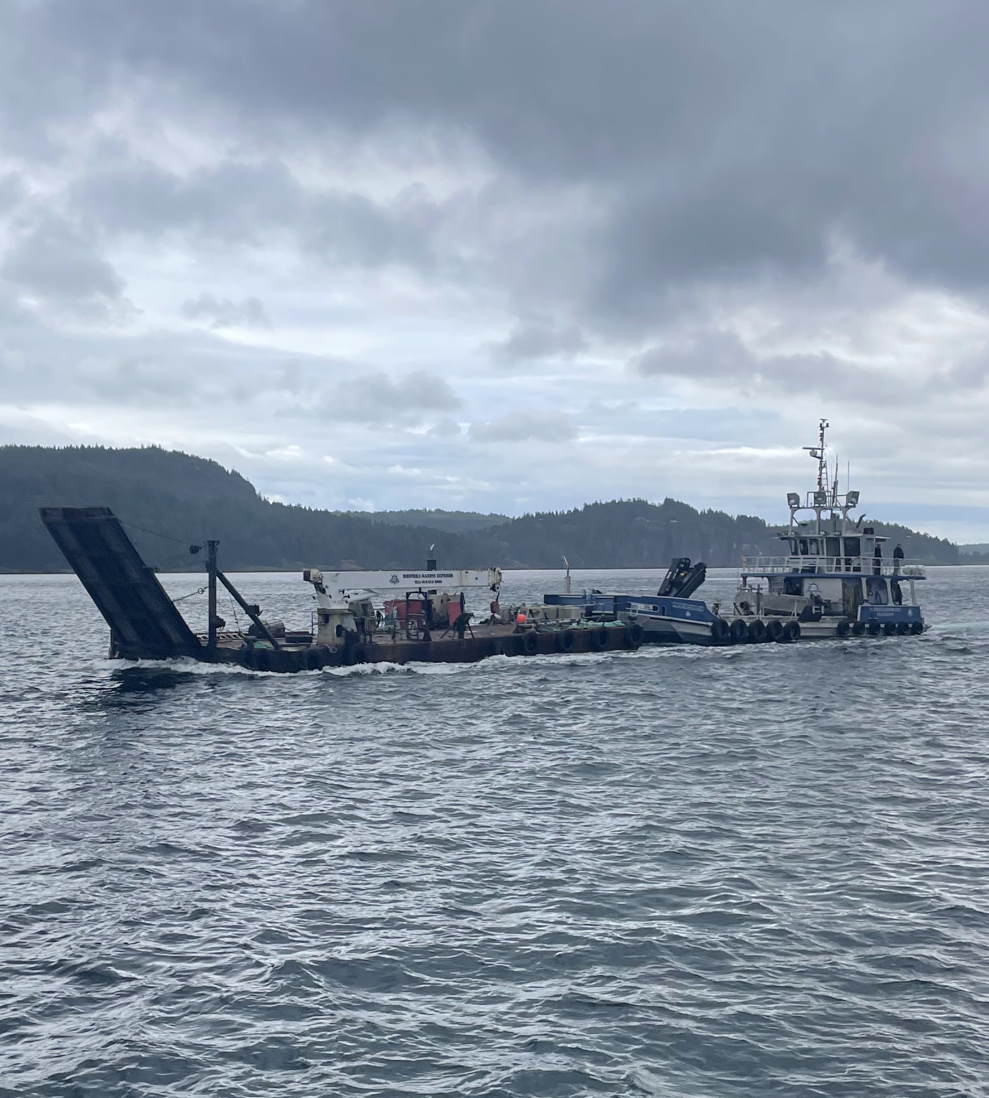 Western Marine Express tug Pacific Spray pushing ramp barge Obelix in a coastal BC marine freight and heavy-lift operation, en route to load cement anchors for dock construction.