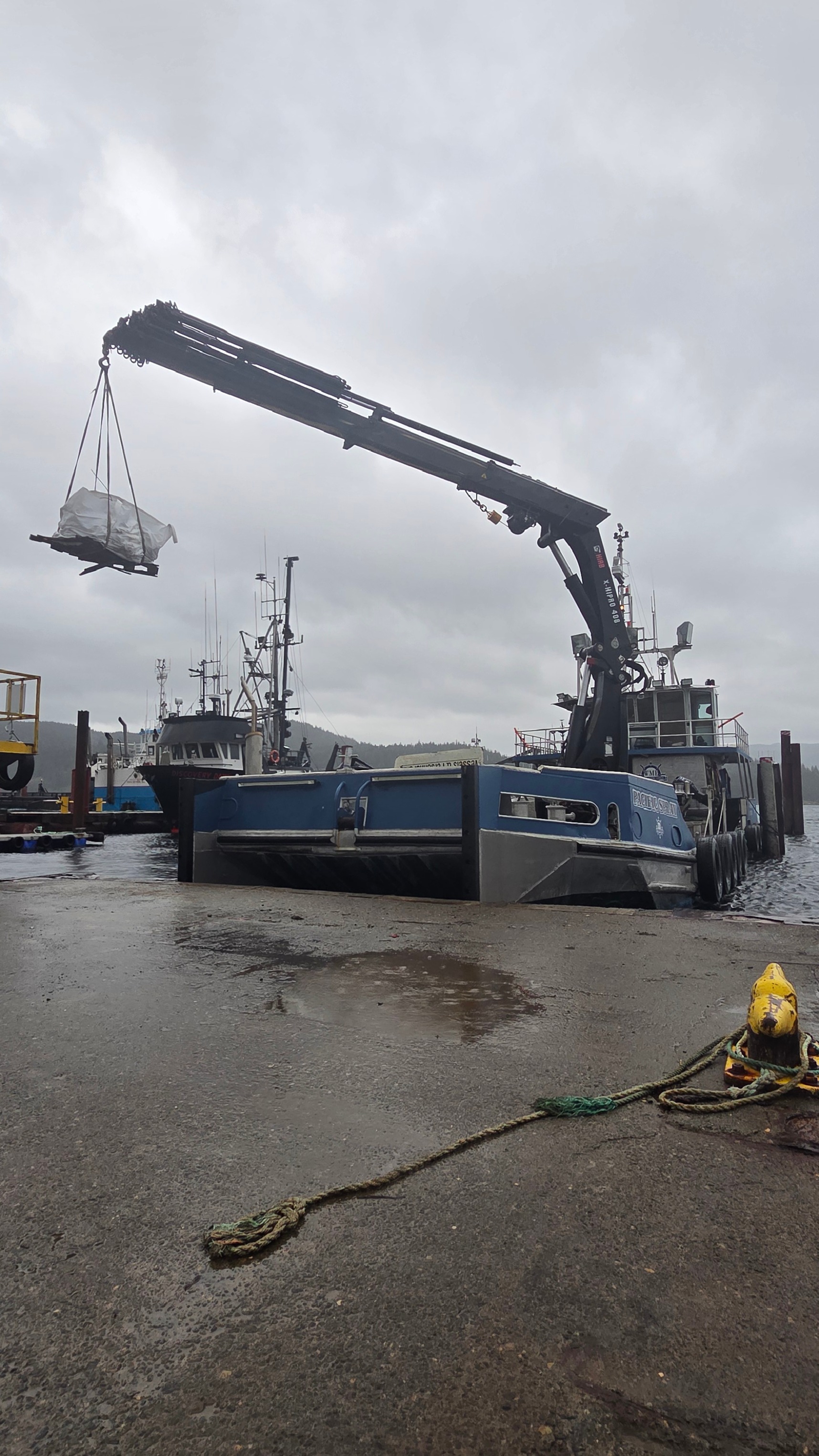 Western Marine Express lifting a 10-ton concrete anchor block with a deck crane during dock installation preparations in Campbell River. The crew specializes in anchoring systems for private docks and marinas.
