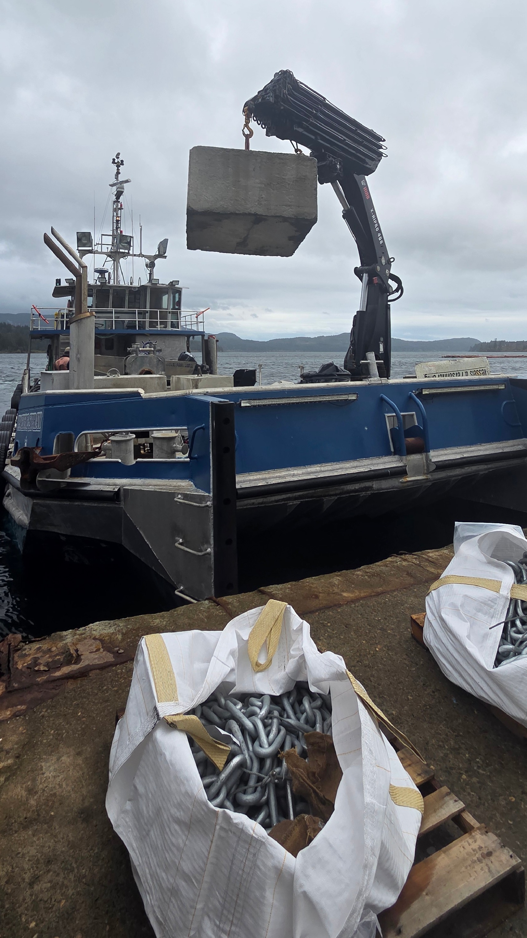 Western Marine Express vessel using a hydraulic crane to load 5-ton dock anchors and chain assemblies, part of their specialized anchoring system service for private docks and marinas.