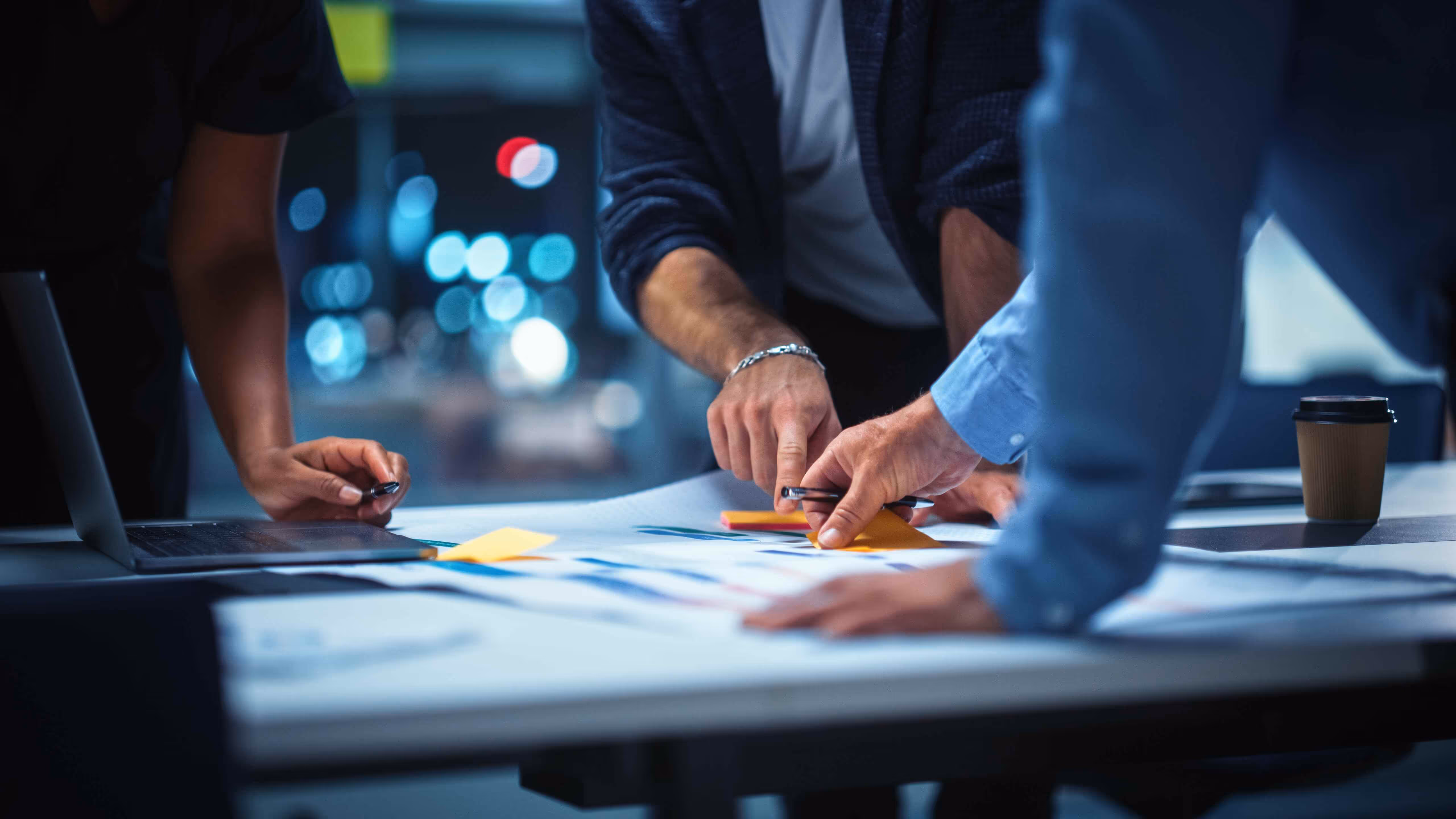 Hands point to documents on a table in a meeting.