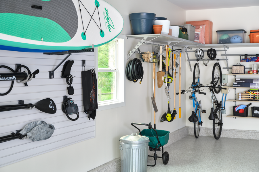Multi-purpose garage storage with mounted bikes, paddleboards, garden tools, and overhead bins arranged for efficient use of space.