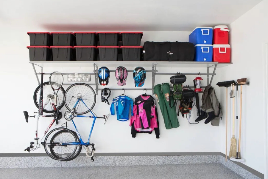 Organized garage wall with overhead storage bins, hanging bikes, helmets, sports gear, and outdoor equipment stored on racks and hooks.