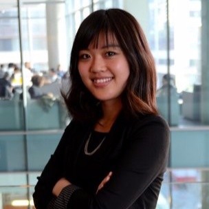 Young woman smiling with arms crossed in a modern office with glass walls.