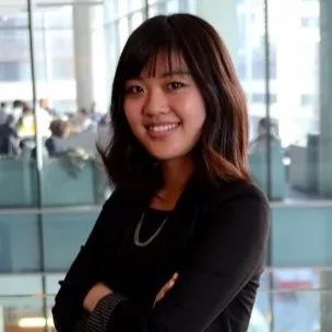 Young woman smiling with arms crossed in a modern office with glass walls.
