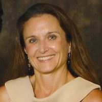 Smiling woman with long brown hair wearing earrings and a sleeveless top against a dark background.