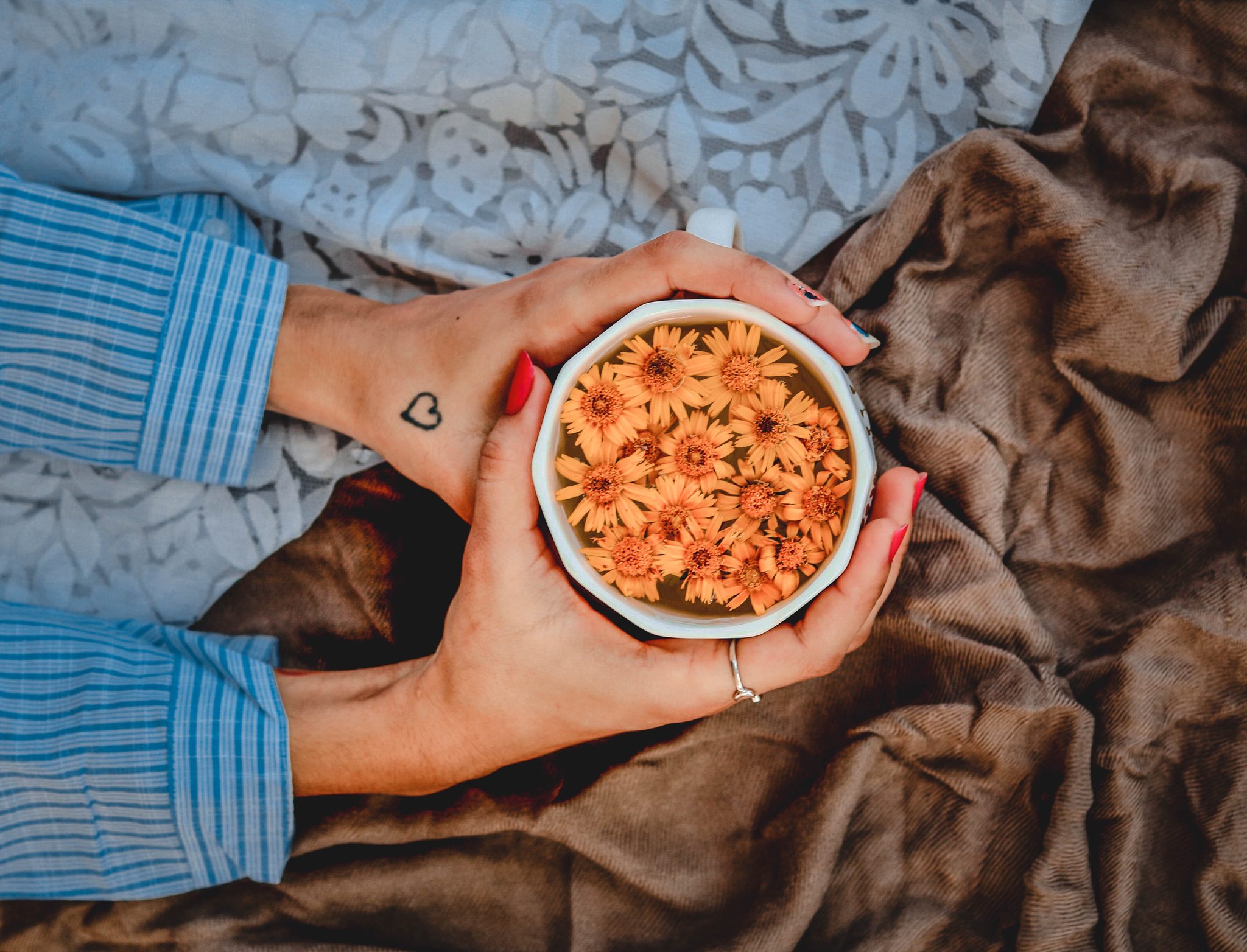 Hands holding a cup of tea with fresh flowers, symbolizing calm and self-care in therapy