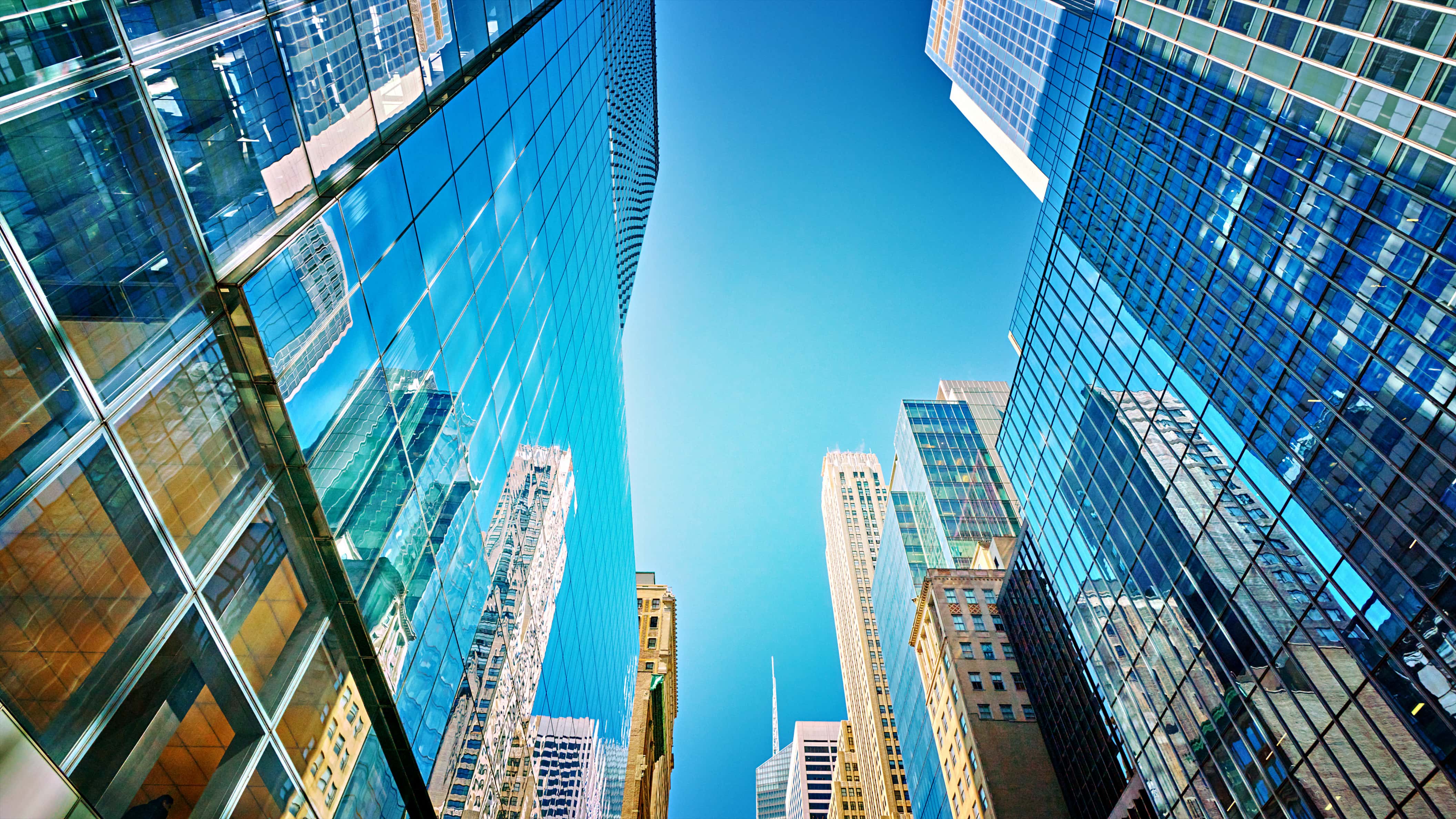 Looking up at a modern city landscape with towering skyscrapers made of reflective blue windows.