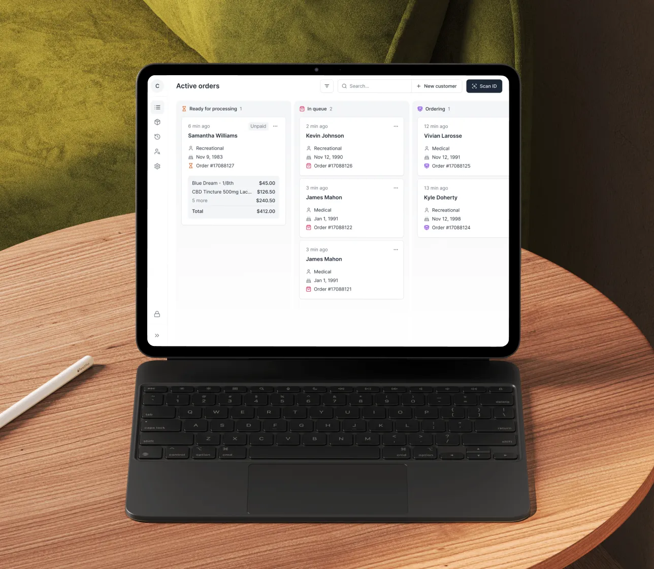 Tablet on wooden table displaying an active orders dashboard with columns for Ready for processing, In queue, and Ordering showing customer names, order details, and timestamps.