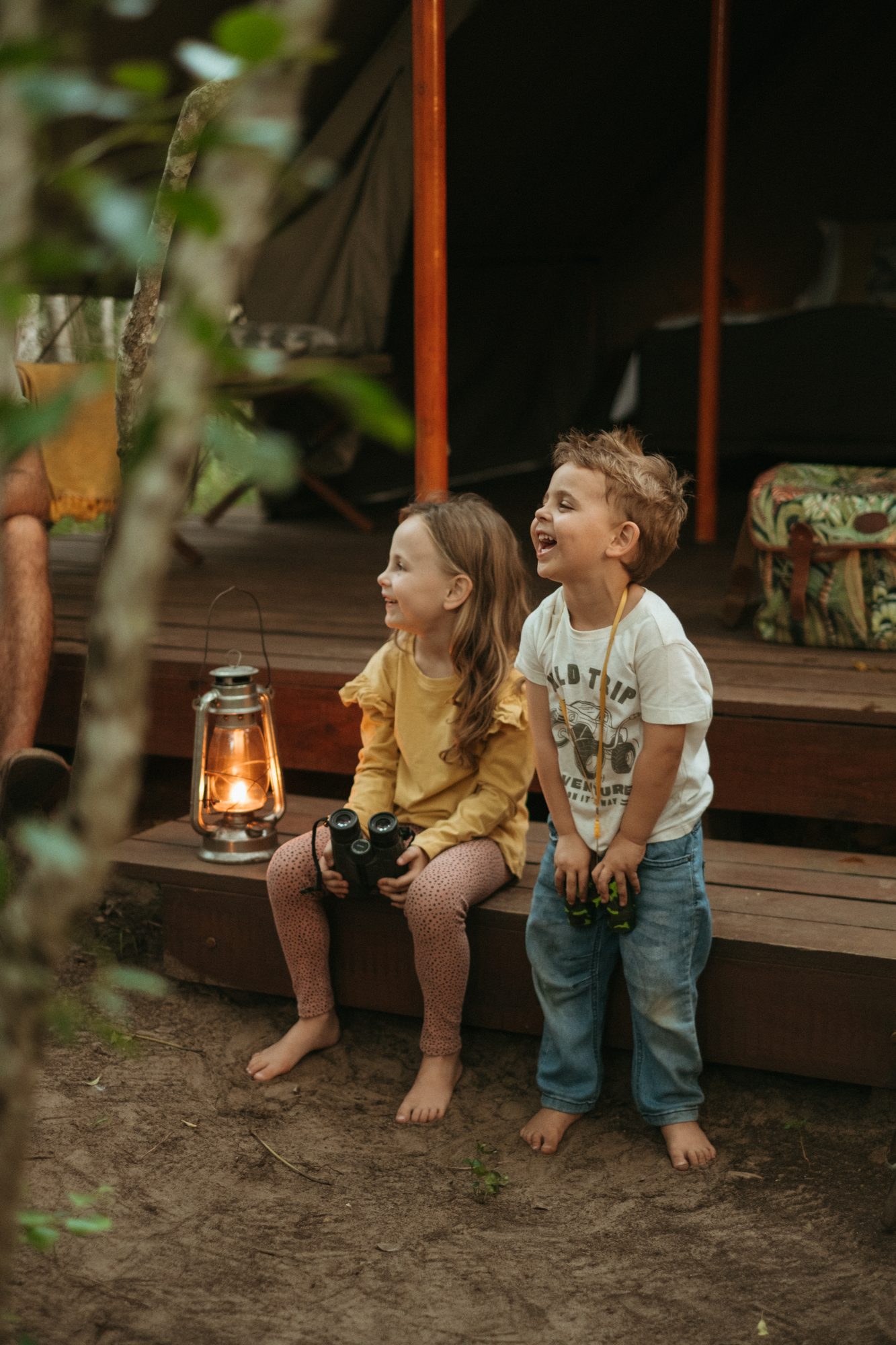Two children laughing on the tent steps with binoculars and a lantern