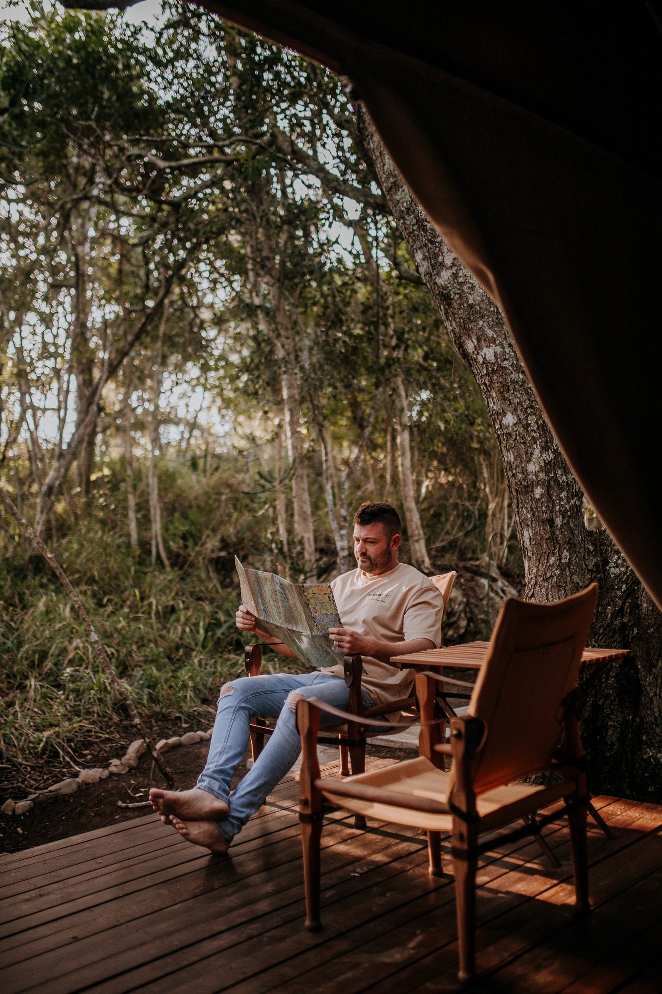A guest reading a map on the tent deck, barefoot under the trees