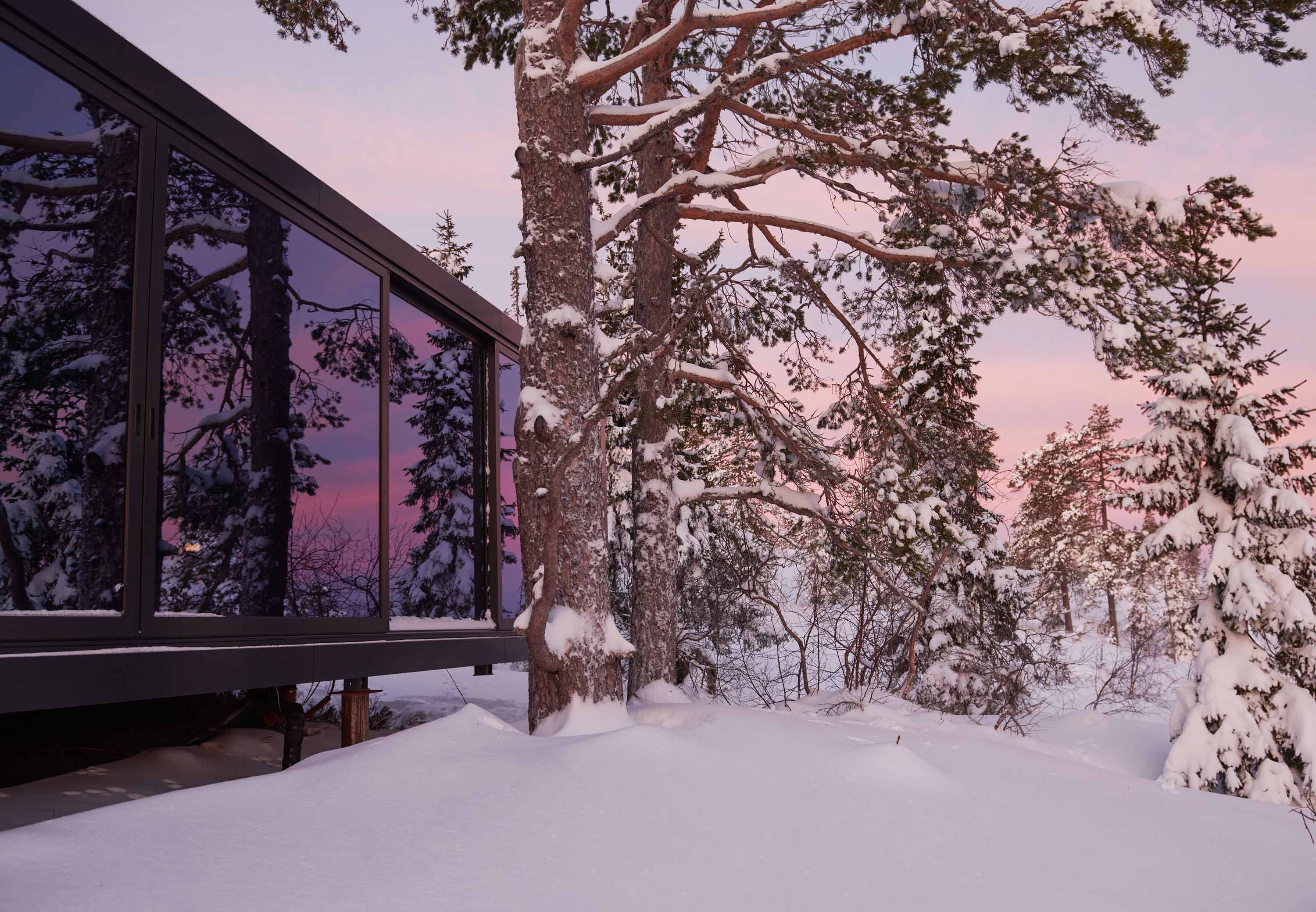 Firkantede hytter stablet oppå hverandre, med utsikt over skogen og solnedgangen.