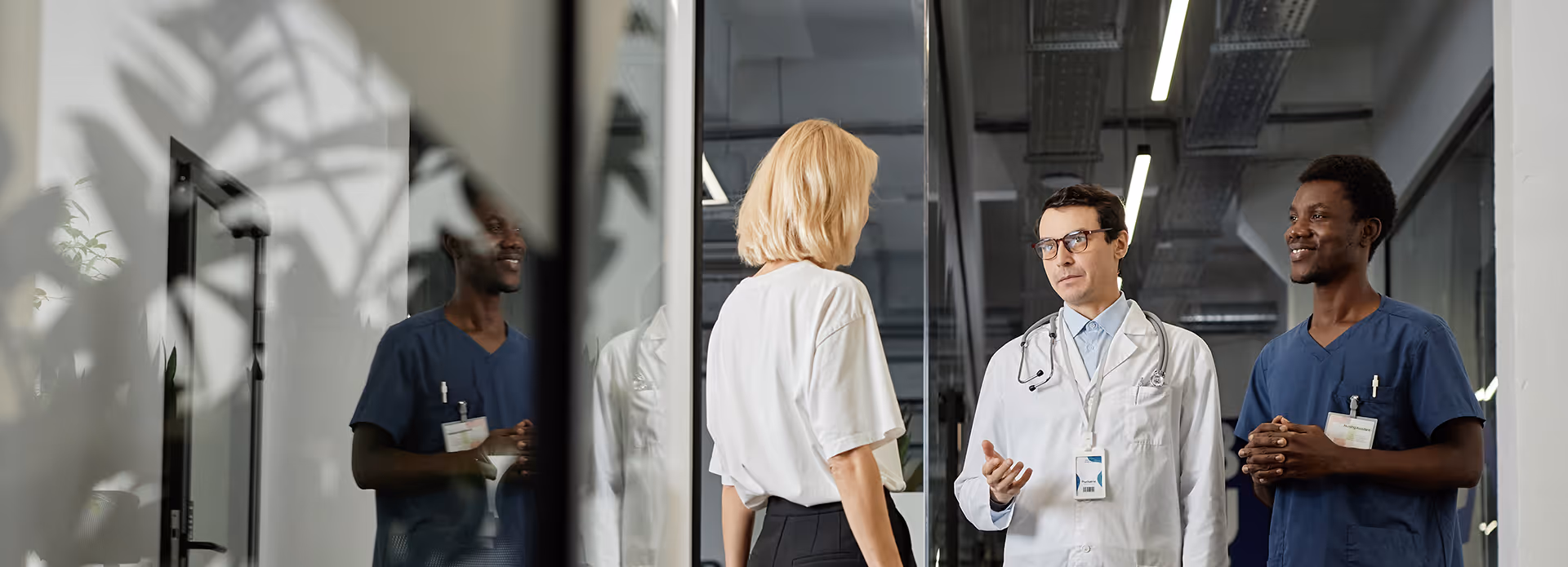 Doctor in lab coat with assistant in blue uniform consulting female patient.