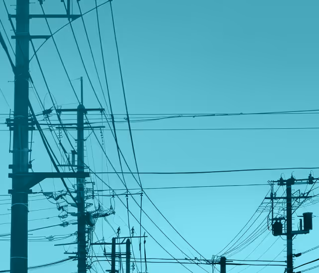 Silhouettes of utility poles and numerous power lines against a clear blue sky.