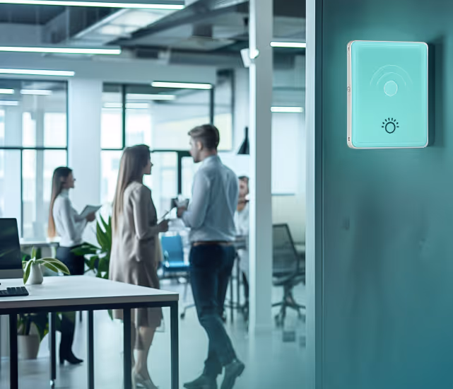 Modern office with people talking in the background and a smart light control panel mounted on a teal wall in the foreground.