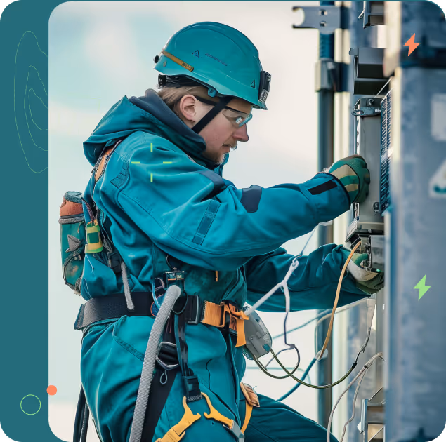 Technician in green safety gear and helmet working on electrical panel with wires.