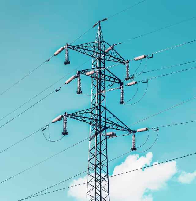 Metal electricity transmission tower with multiple power lines against a bright blue sky with a few clouds.