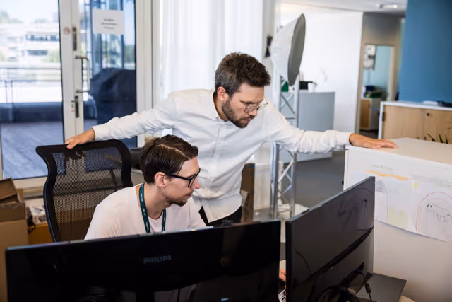 Two men working together at computer monitors in a modern office with natural light.