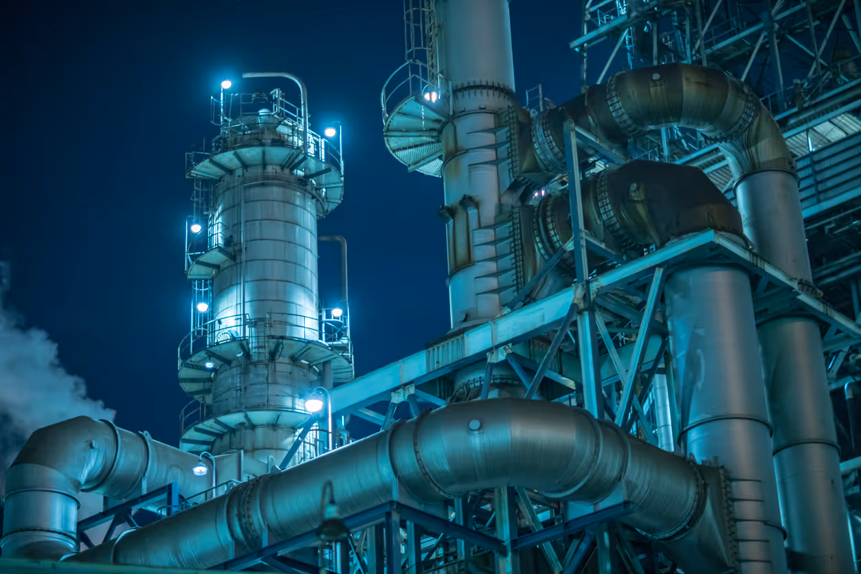Industrial refinery or chemical plant with large metal pipes and towers illuminated at night.