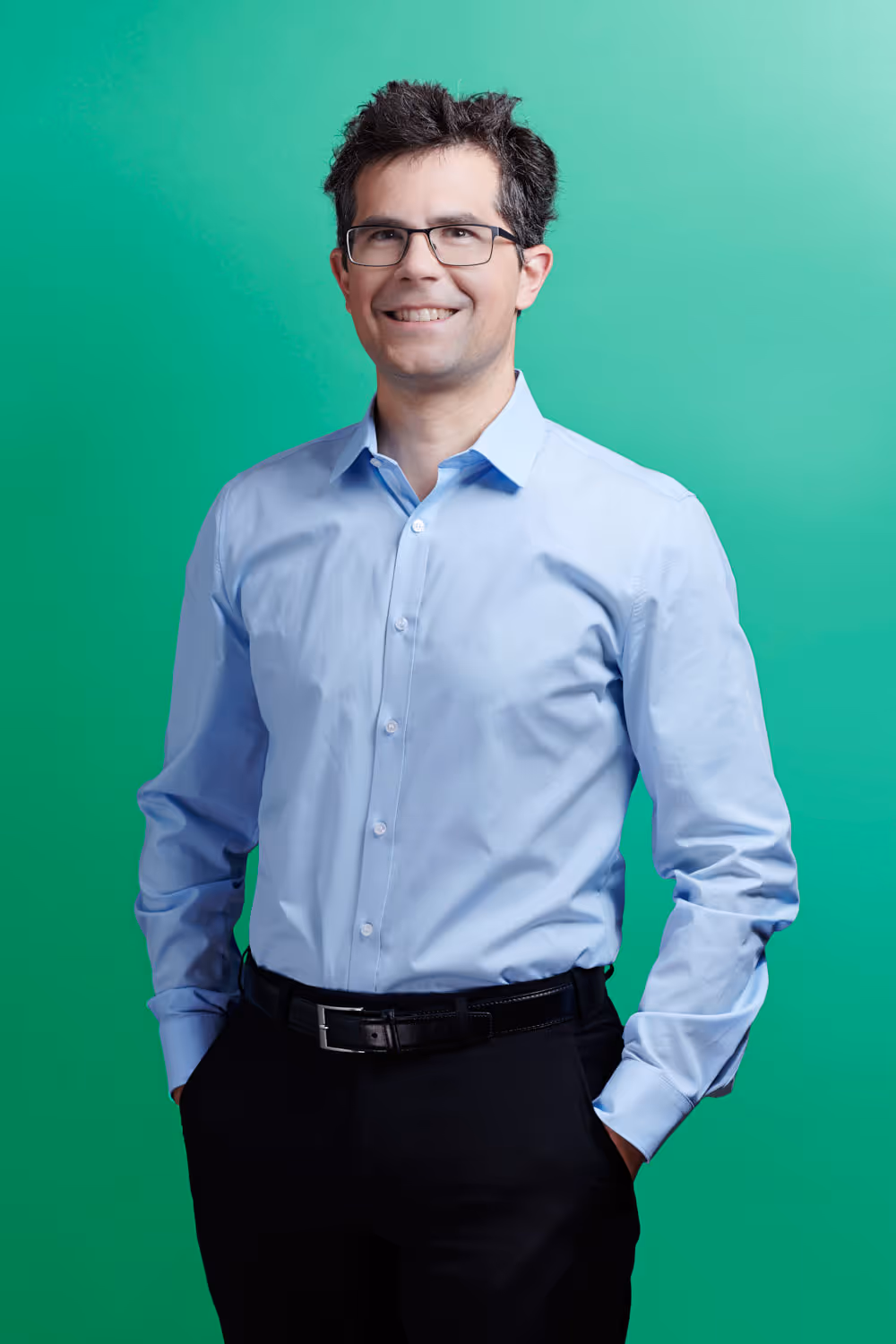 Der Rechtsanwalt Dr. Gian Sandro Genna steht vor farbigem Studiohintergrund und schaut freundlich in die Kamera.