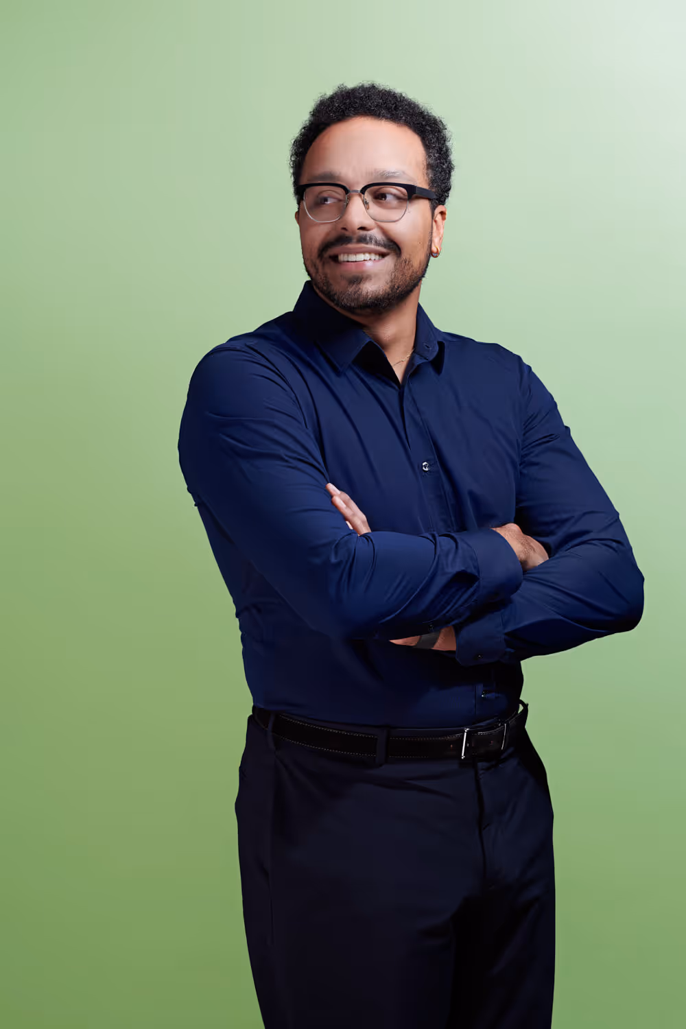 Der Rechtsanwalt Patrice Kazadi von Jusonline steht mit verschränkten Armen vor farbigem Studiohintergrund.