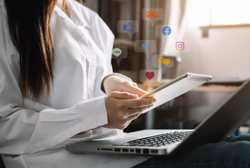 Socialinės žiniasklaidos ir rinkodaros virtualių piktogramų ekranas, kuriame verslininkės namuose rašo klaviatūra su nešiojamuoju kompiuteriu ir planšetiniu kompiuteriu