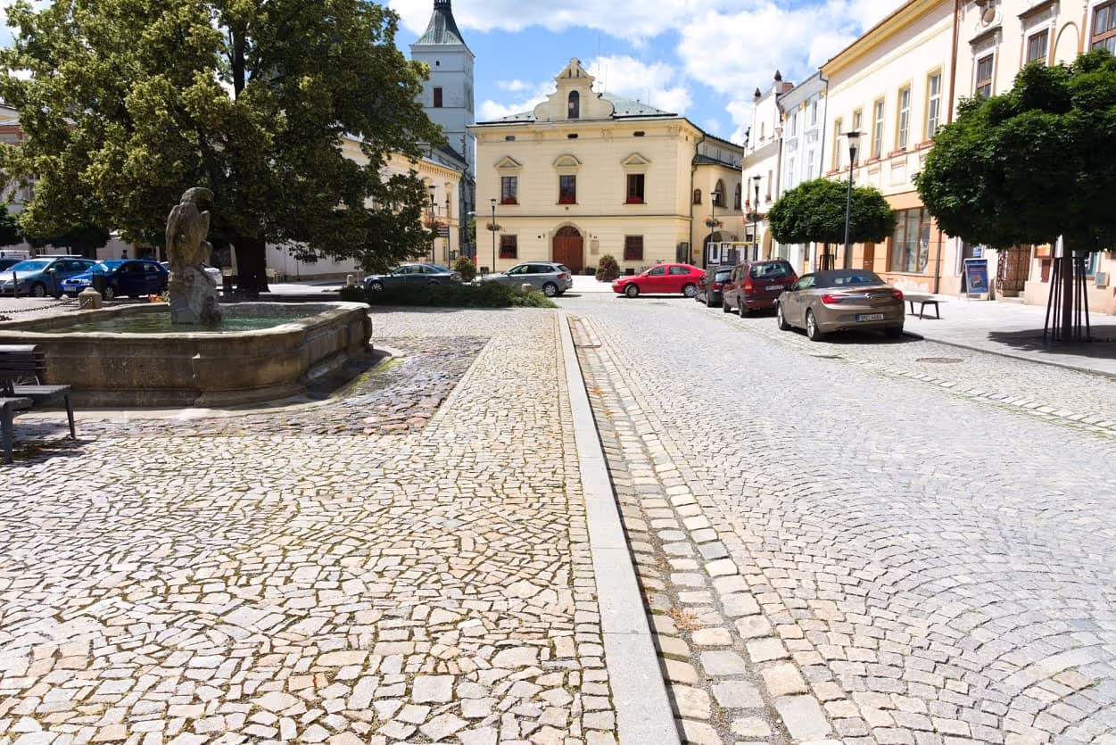 Historické uničovské náměstí s kamennou kašnou, žulovými odseky a kostkami, lemované žulovým obrubníkem.
